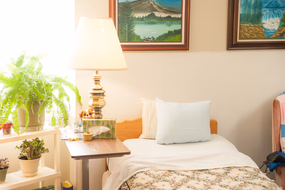 Cozy senior facility bedroom with a bed, lamp, and potted plants.