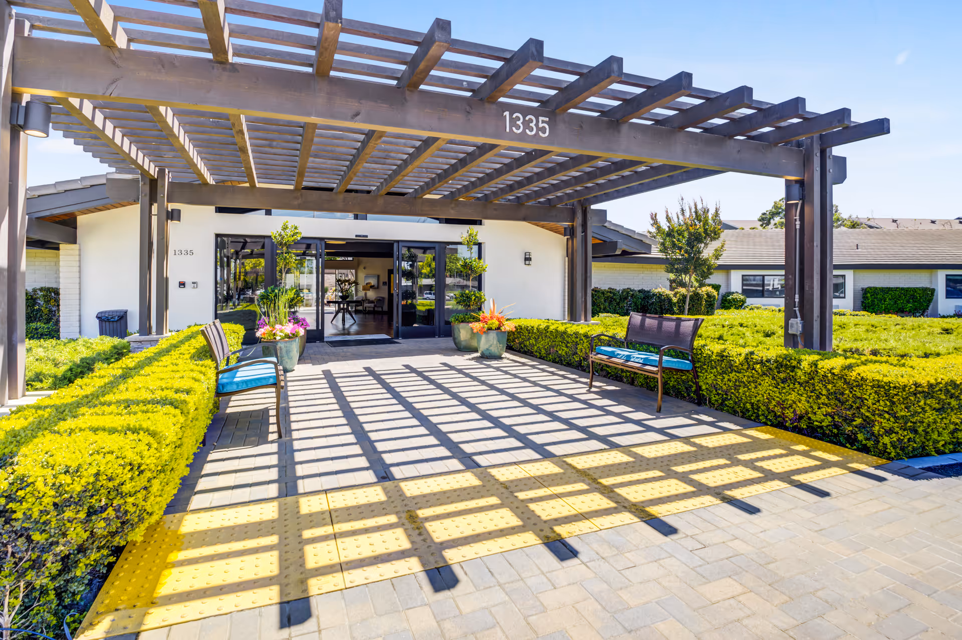 Entrance of Madonna Gardens Assisted Living and Memory Care with a wooden pergola and benches.