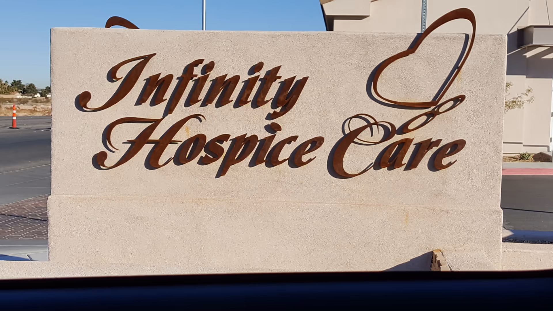 A beige stone sign reads Infinity Hospice Care with cursive lettering in front of a building.