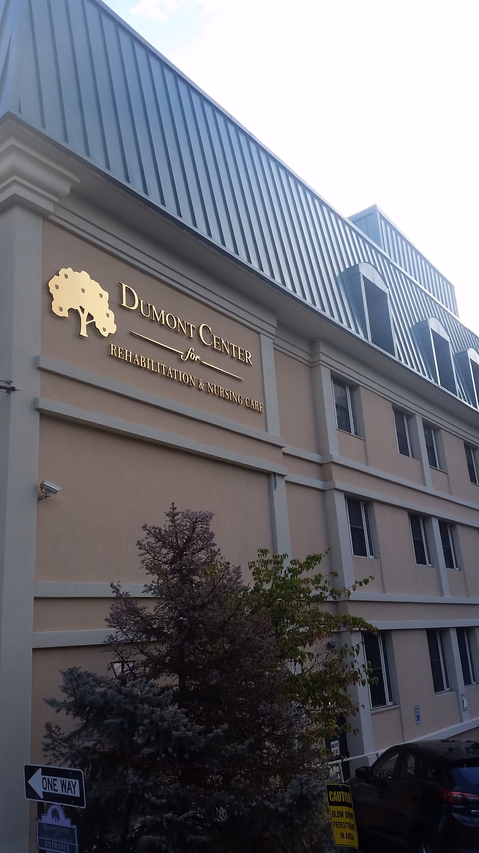 Exterior view of a beige building with a Dumont Center sign and landscaping.
