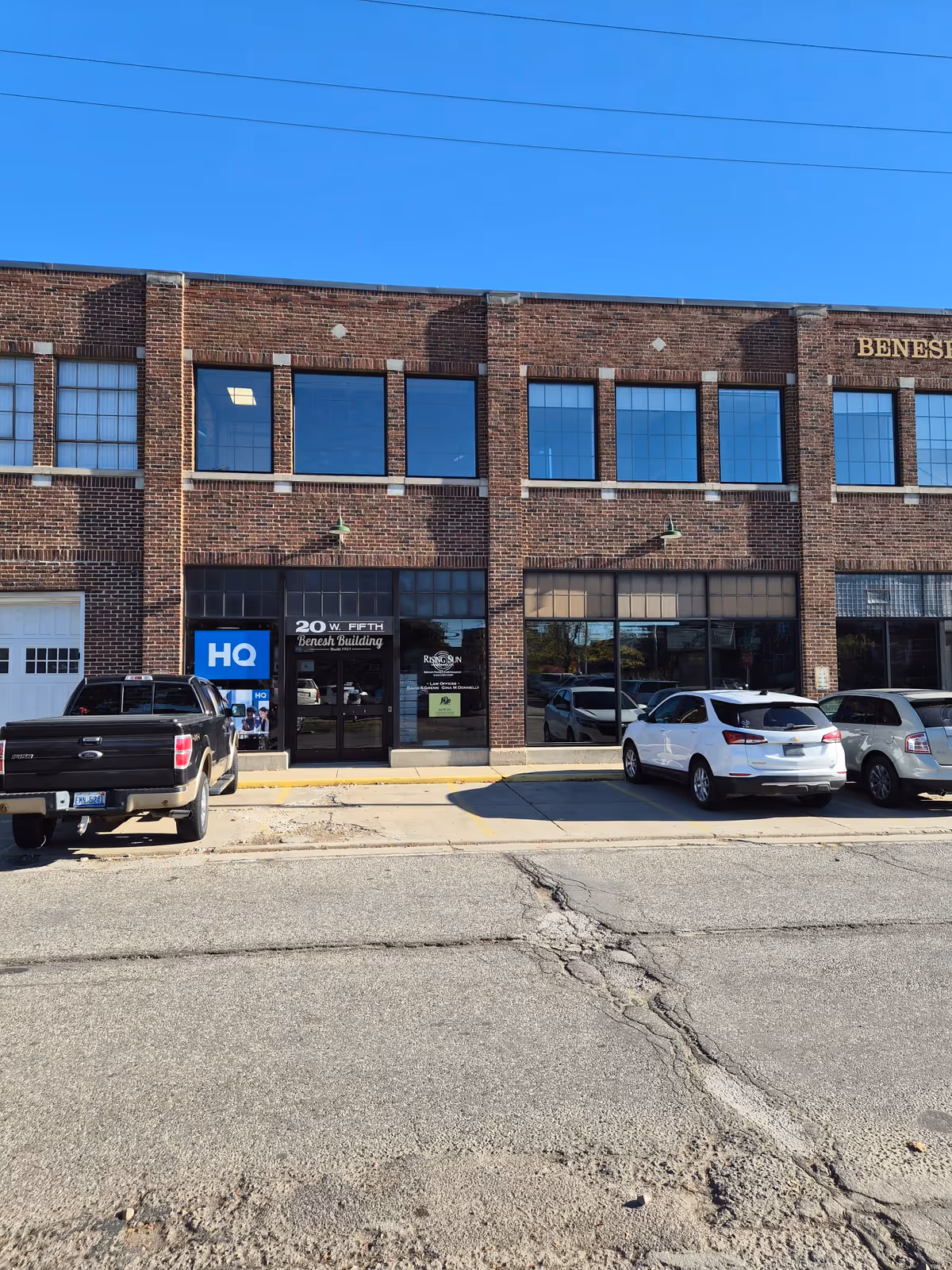 Brick commercial building with storefront windows and parked cars in front.
