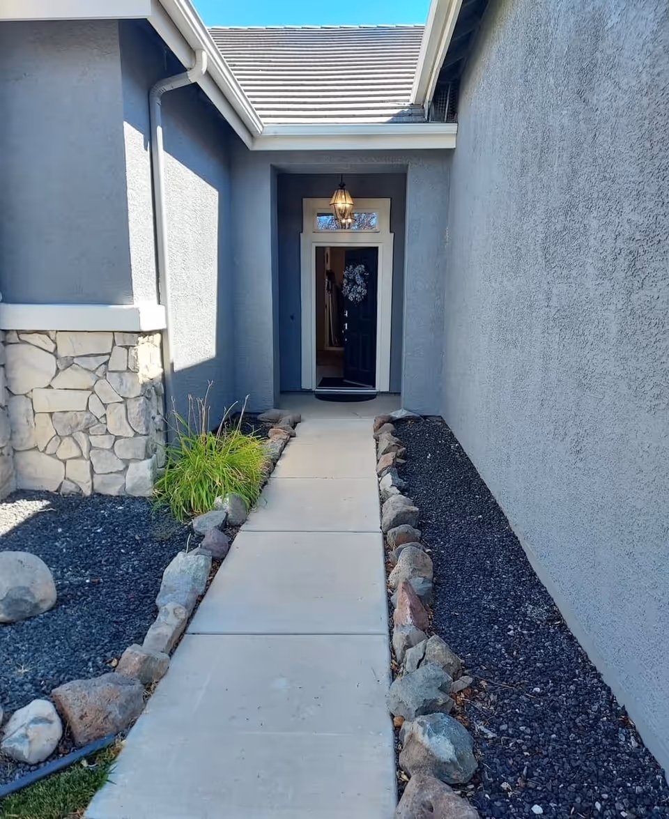 Gray exterior entry with a blue door, lantern light, and rock-lined walkway.