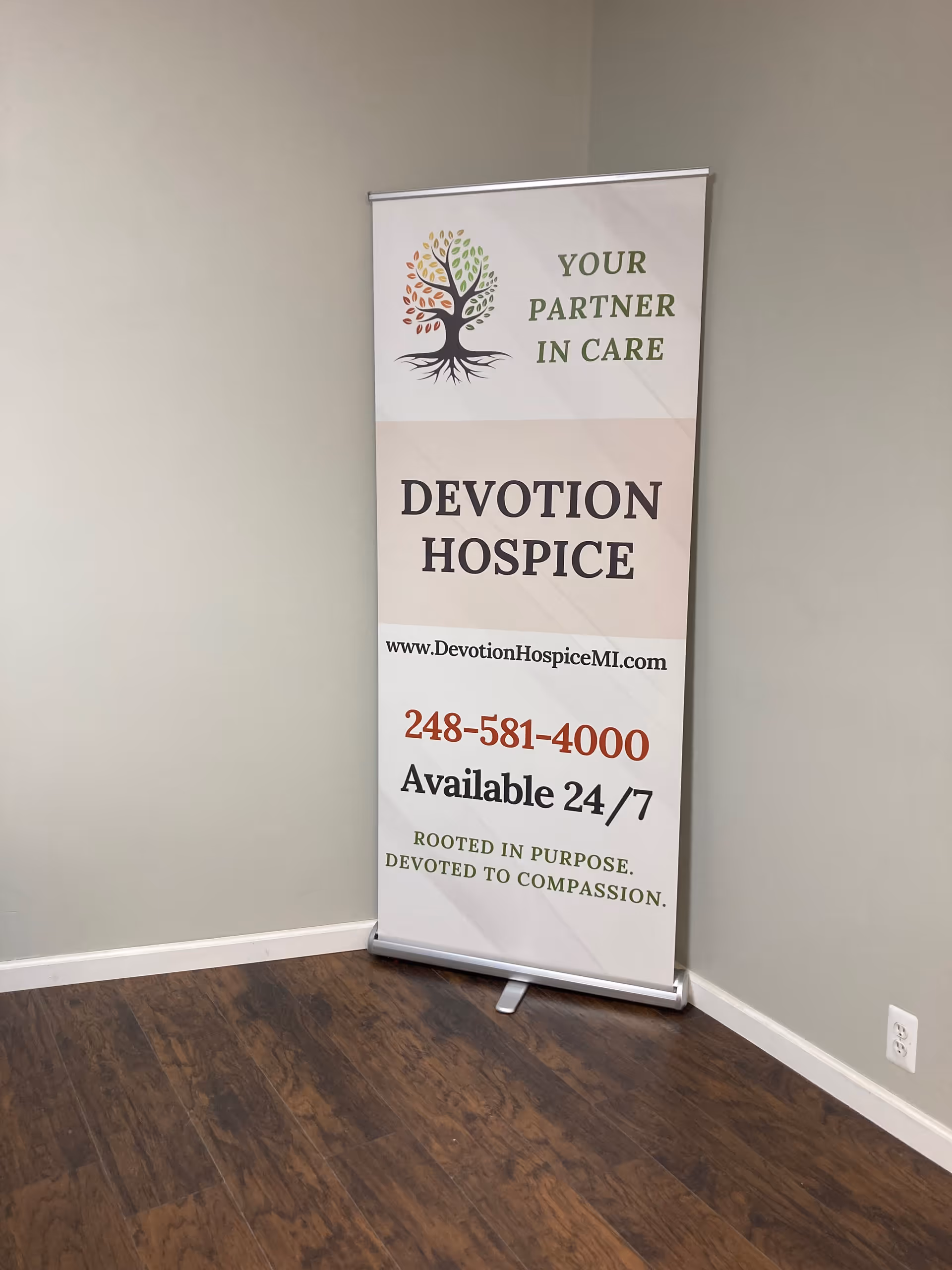 Indoor banner advertising Devotion Hospice with contact information beside a wall.