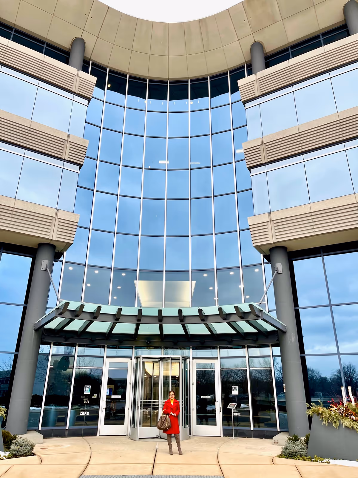 Glass-fronted building entrance with a person standing outside wearing a red coat.