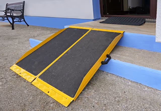 Yellow accessibility ramp leads to a building entrance with a bench nearby.