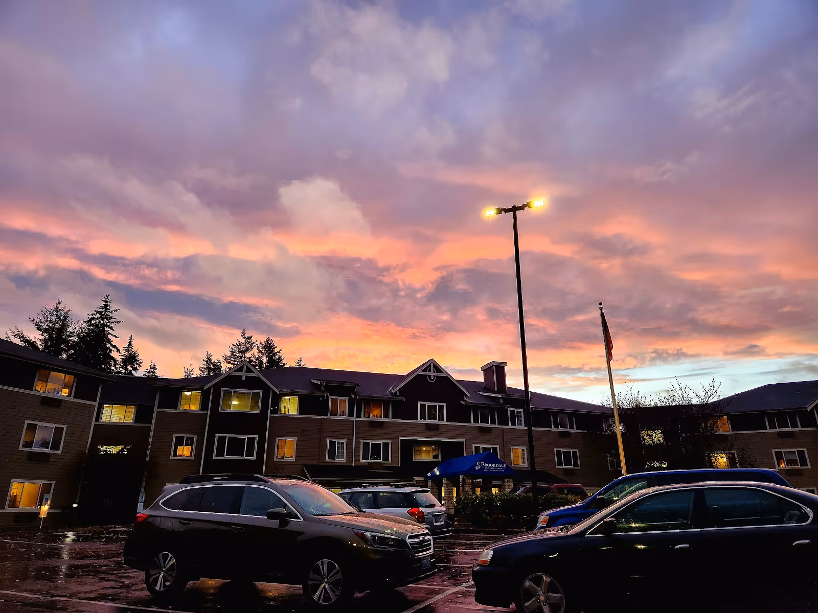 Exterior view of Brookdale Courtyard Puyallup building with parked cars at sunset.