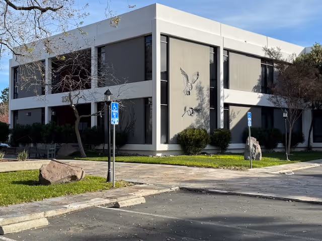 Two-story building with large windows, handicap parking signs, and a bird mural.