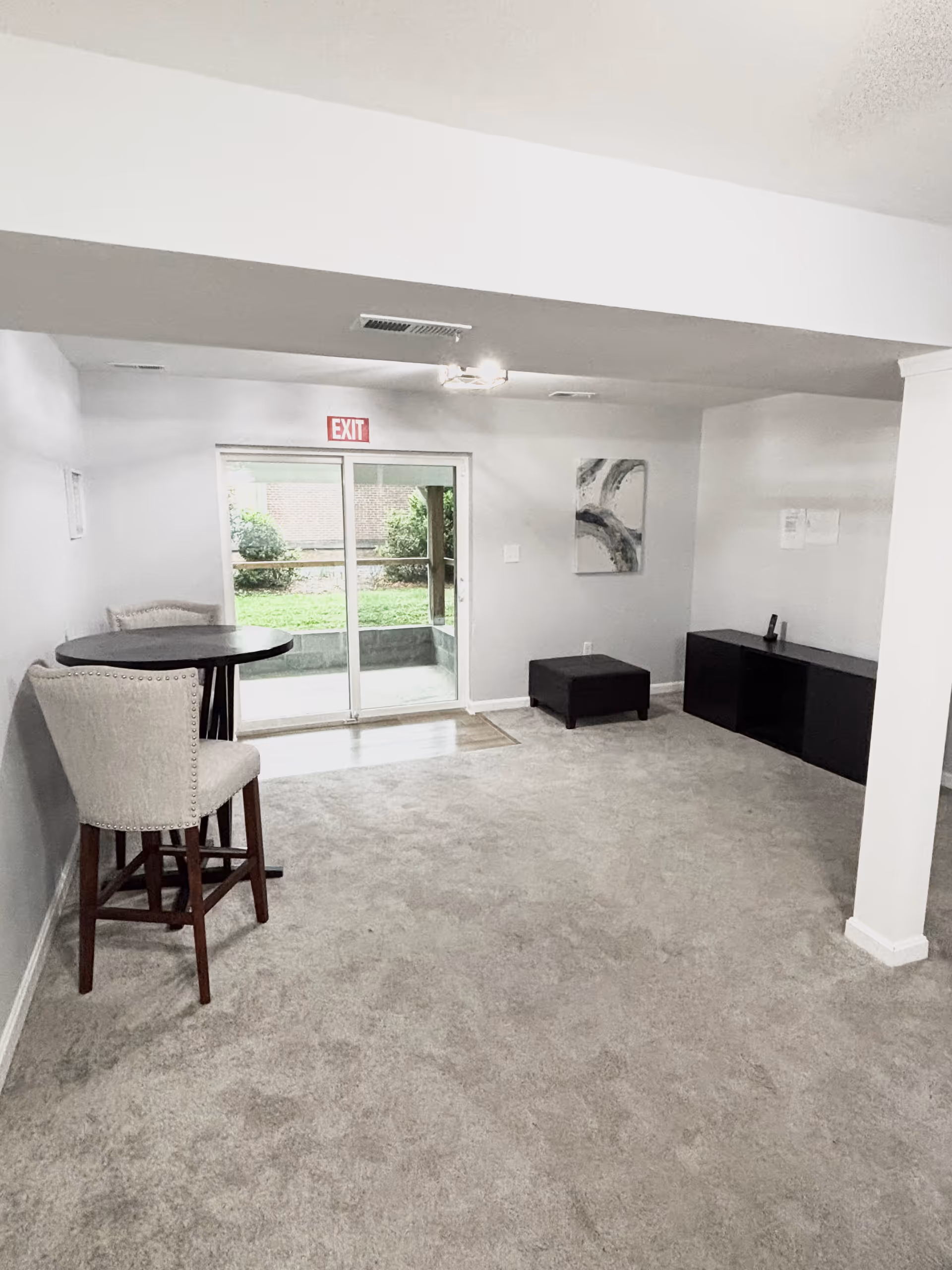 Interior common room with a round table, two tall chairs, and a sliding door to outdoors.