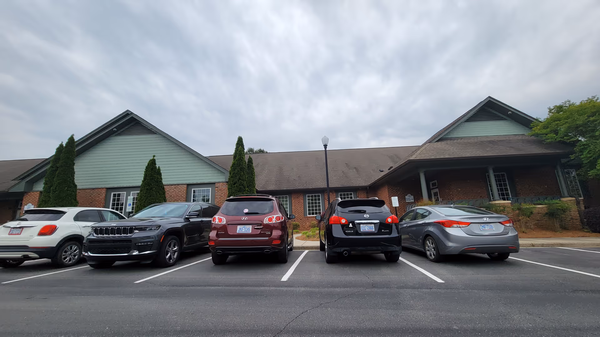 Front exterior of Trellis Supportive Care with cars parked in front, cloudy sky.