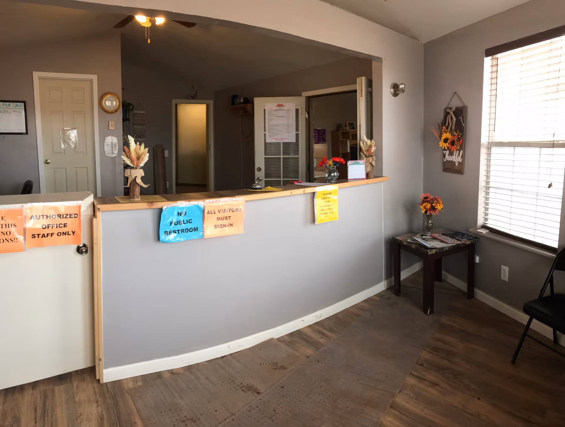Interior reception area with a counter, signs, decorations, and a windowed seating area.