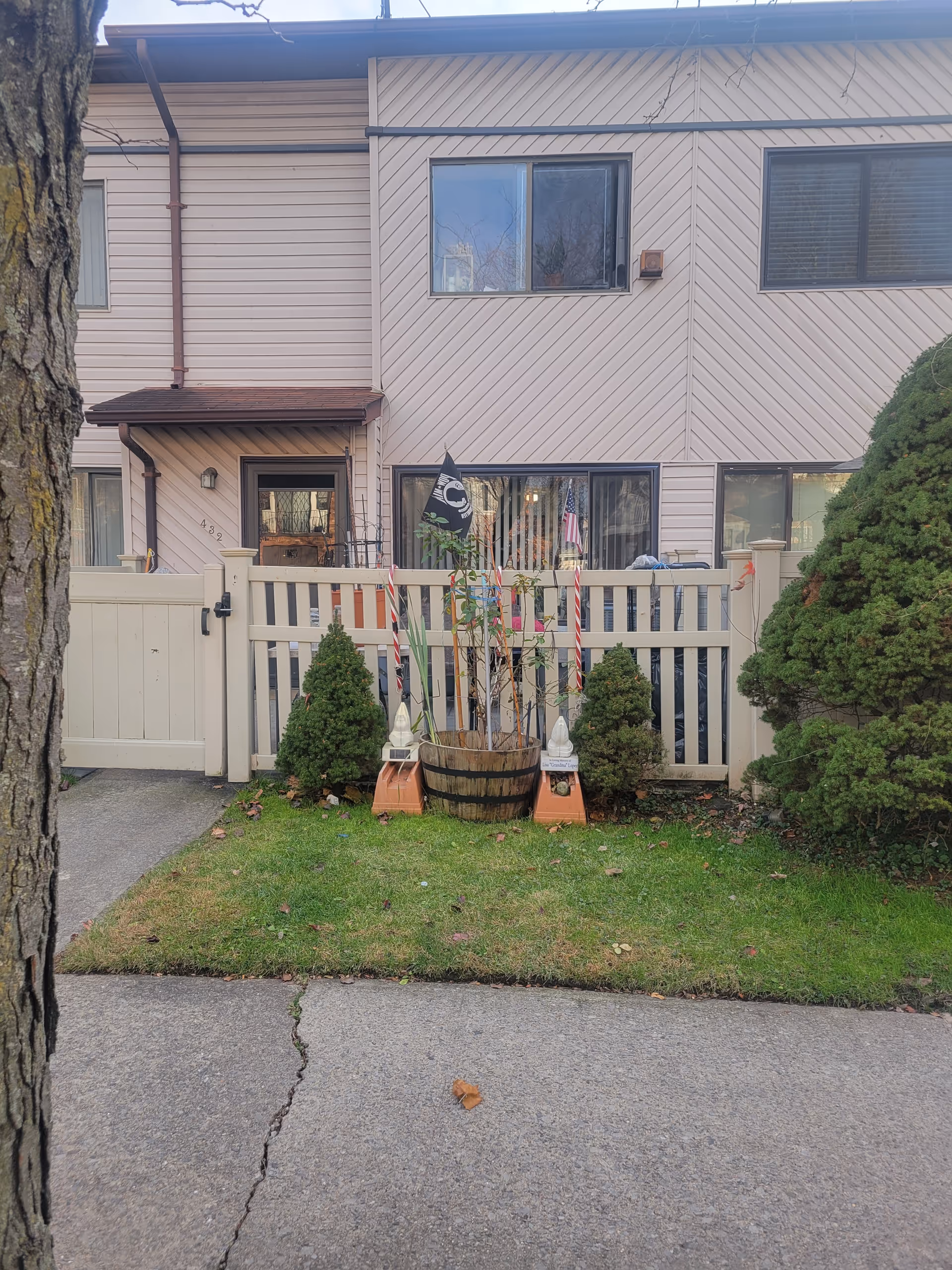 Two-story beige building facade with a white fence, potted decorations, and small shrubs in front.