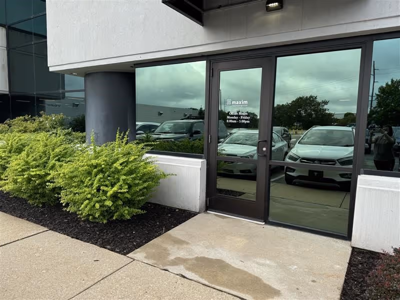 Front entrance of Maxim Healthcare Services building with glass doors and parked cars.