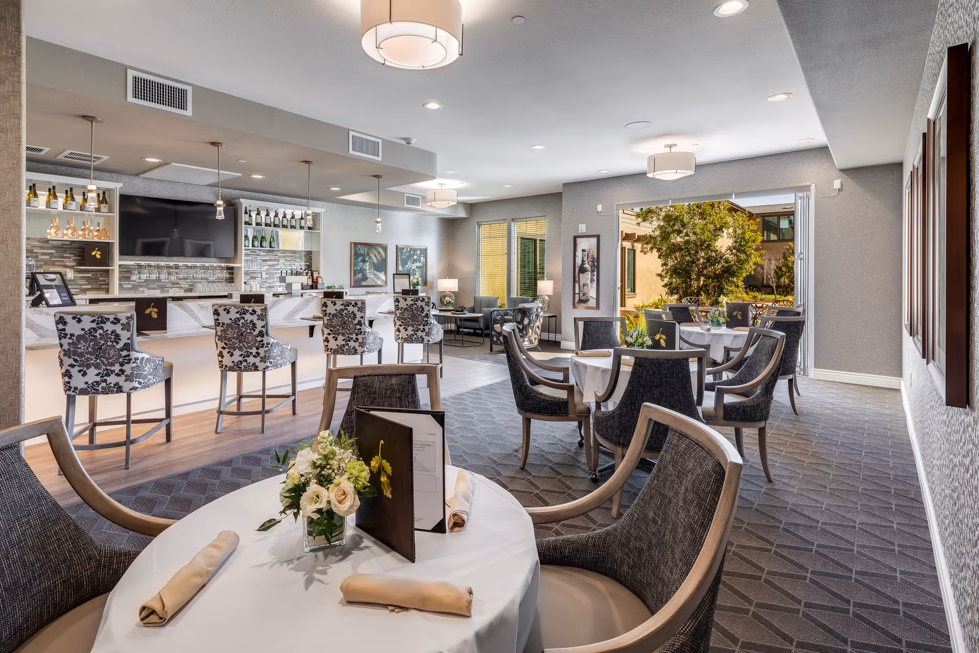 Modern senior living dining and lounge area with a bar and outdoor view.