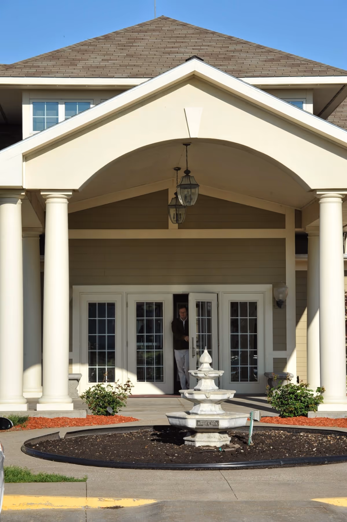 Cream-colored senior living facility entrance with columns, glass doors, and a fountain.