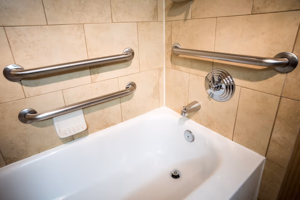 Accessible bathroom with beige tiles and multiple safety grab bars around a bathtub.