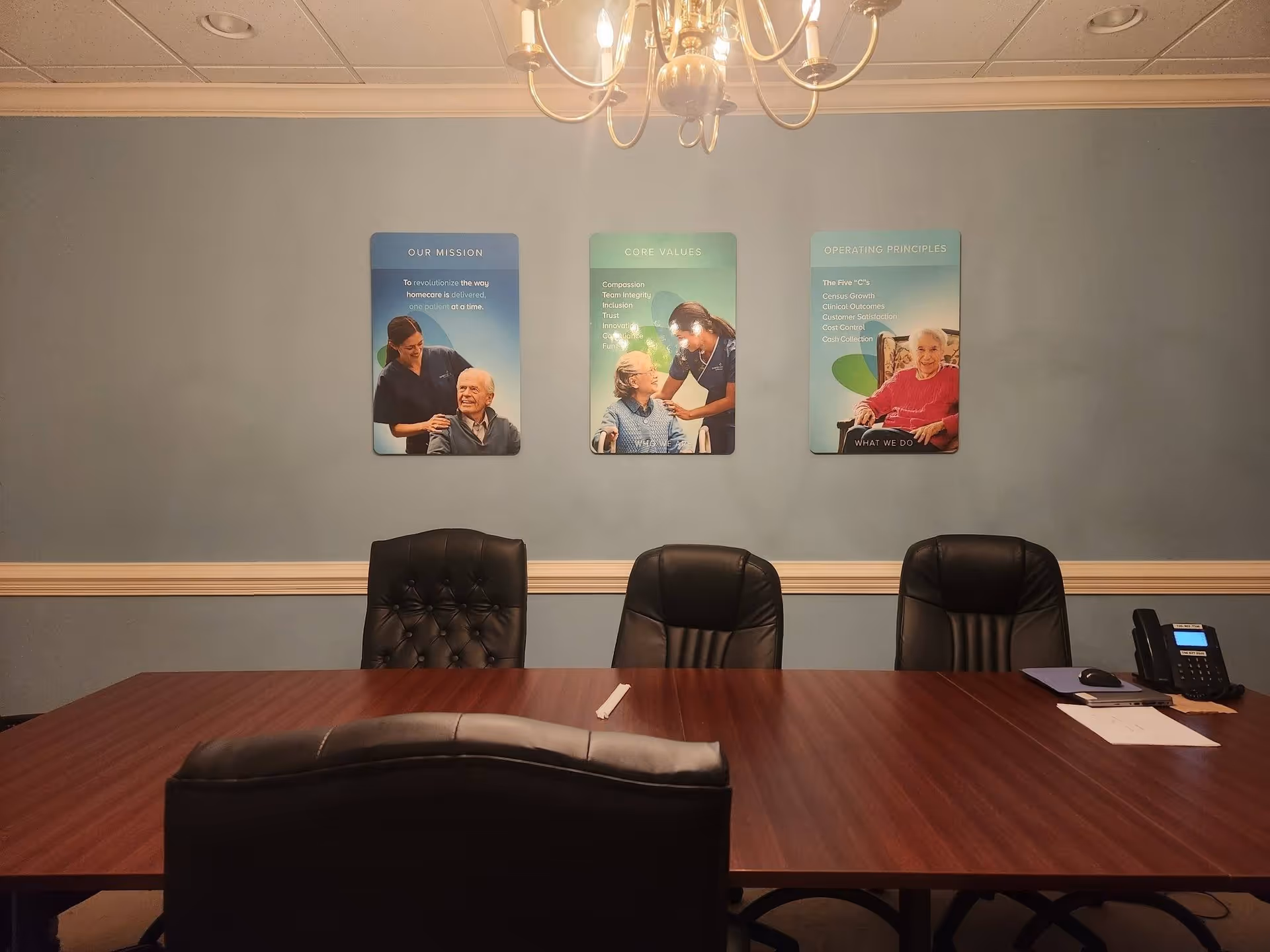 A conference room with a long wooden table, chairs, and wall-mounted posters.