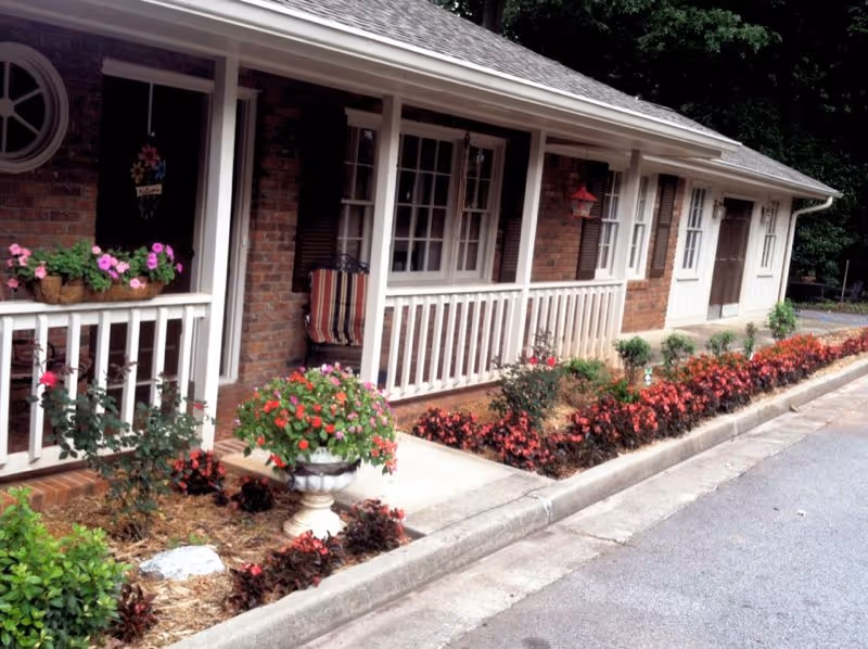 Hembree Senior Care Center exterior with a covered porch, white railing, and blooming flowers.