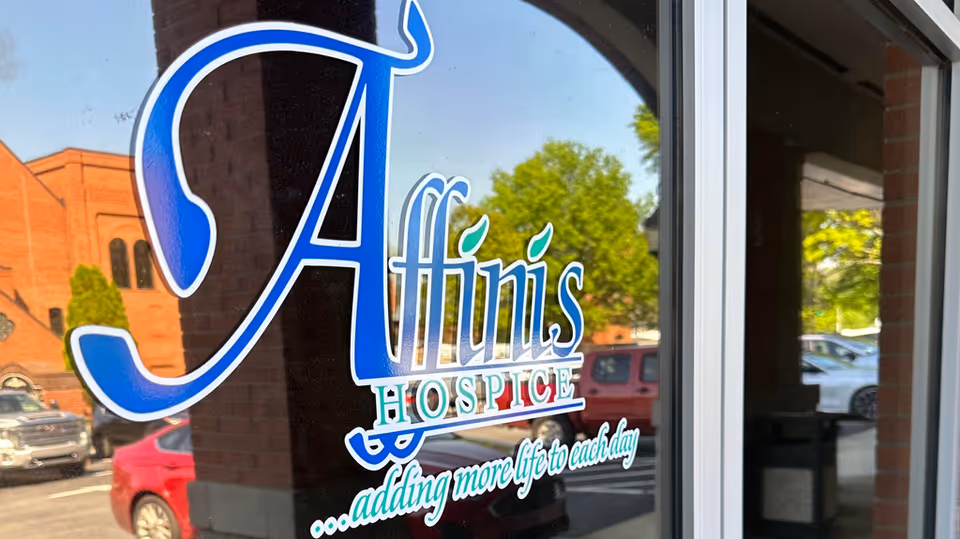 Glass door featuring the Affinis Hospice logo with reflections of parked cars outside