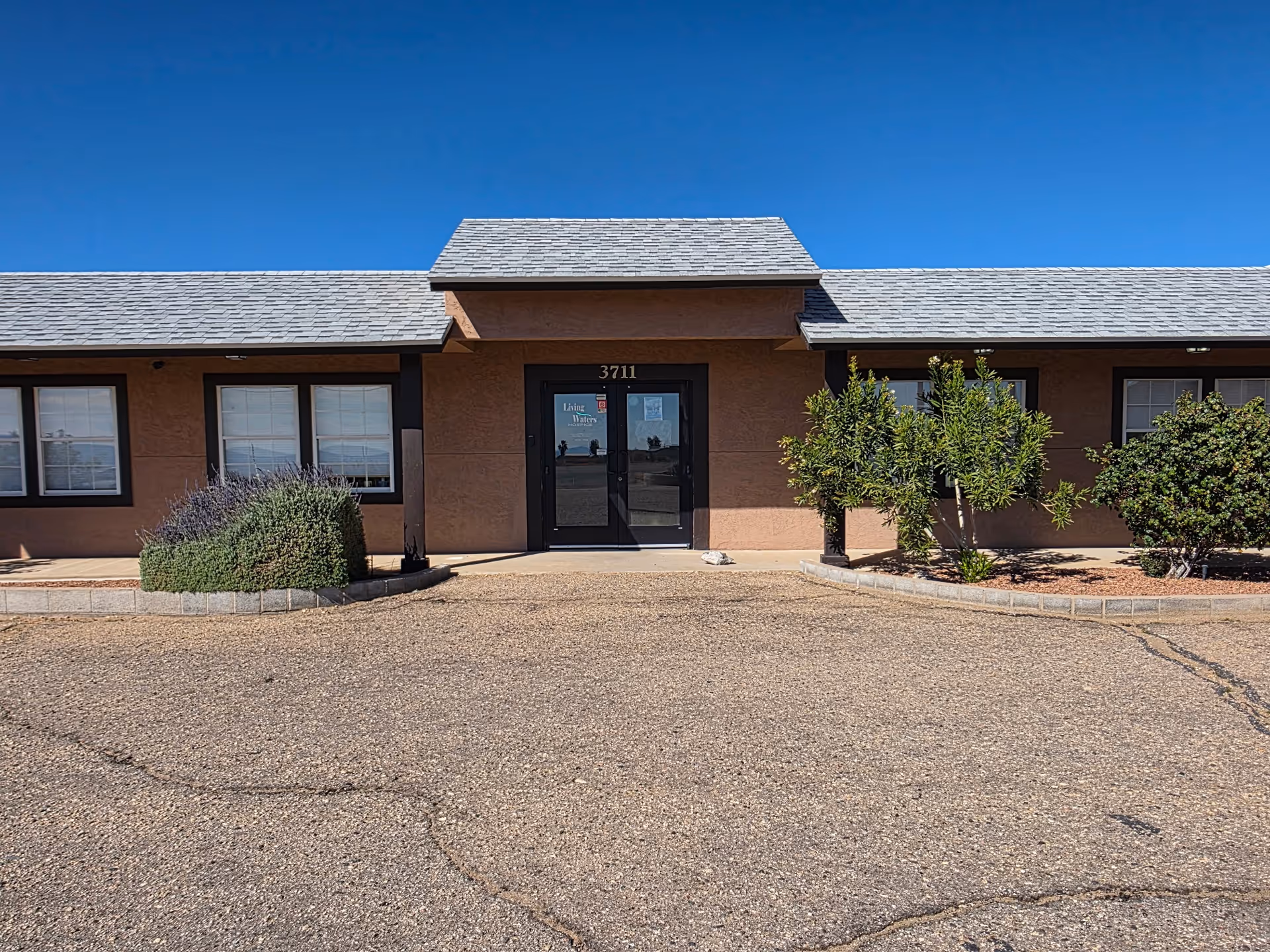 One-story brown building front with glass doors and small landscaped shrubs.