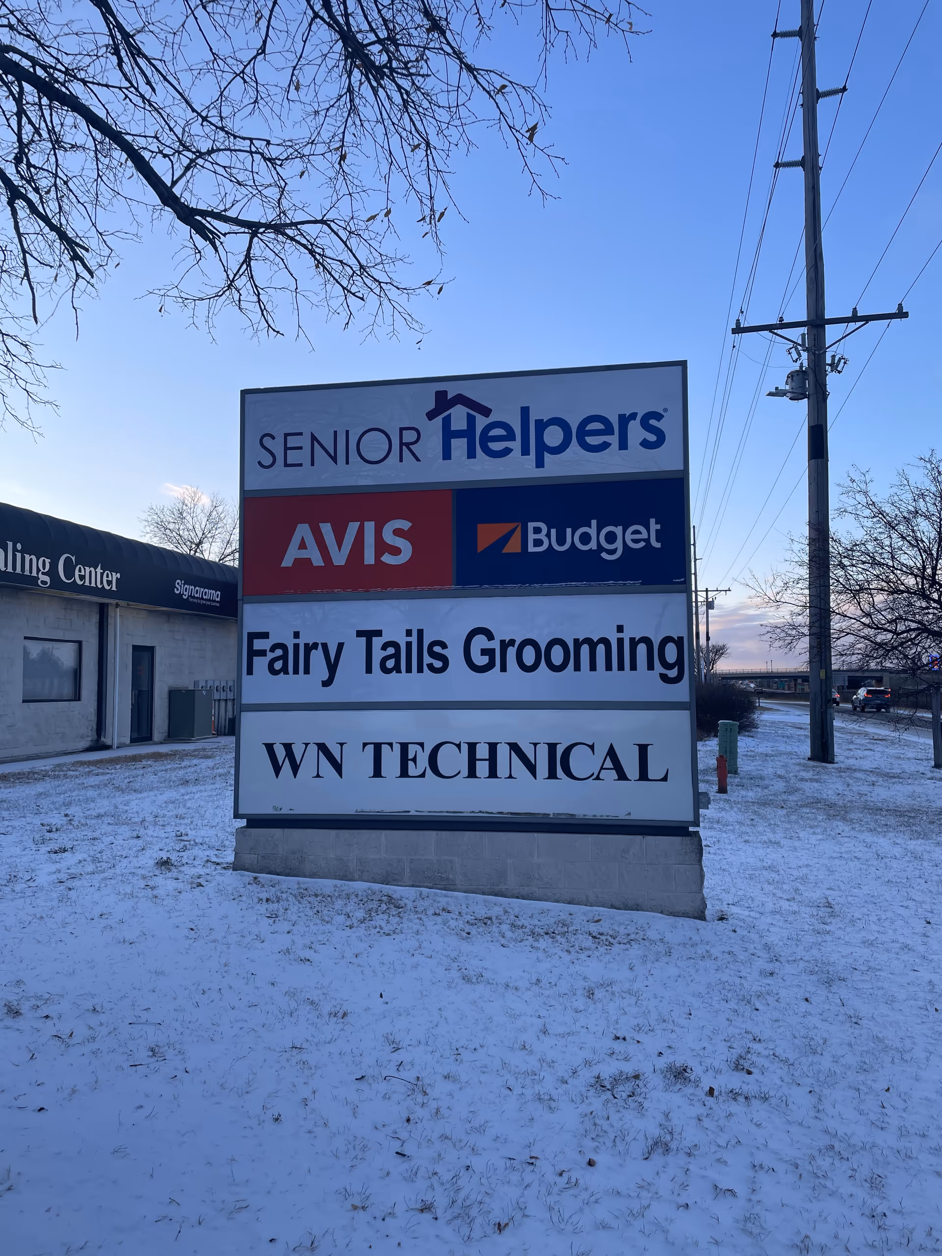 Outdoor signboard displays Senior Helpers North Metro with other business banners in snow.