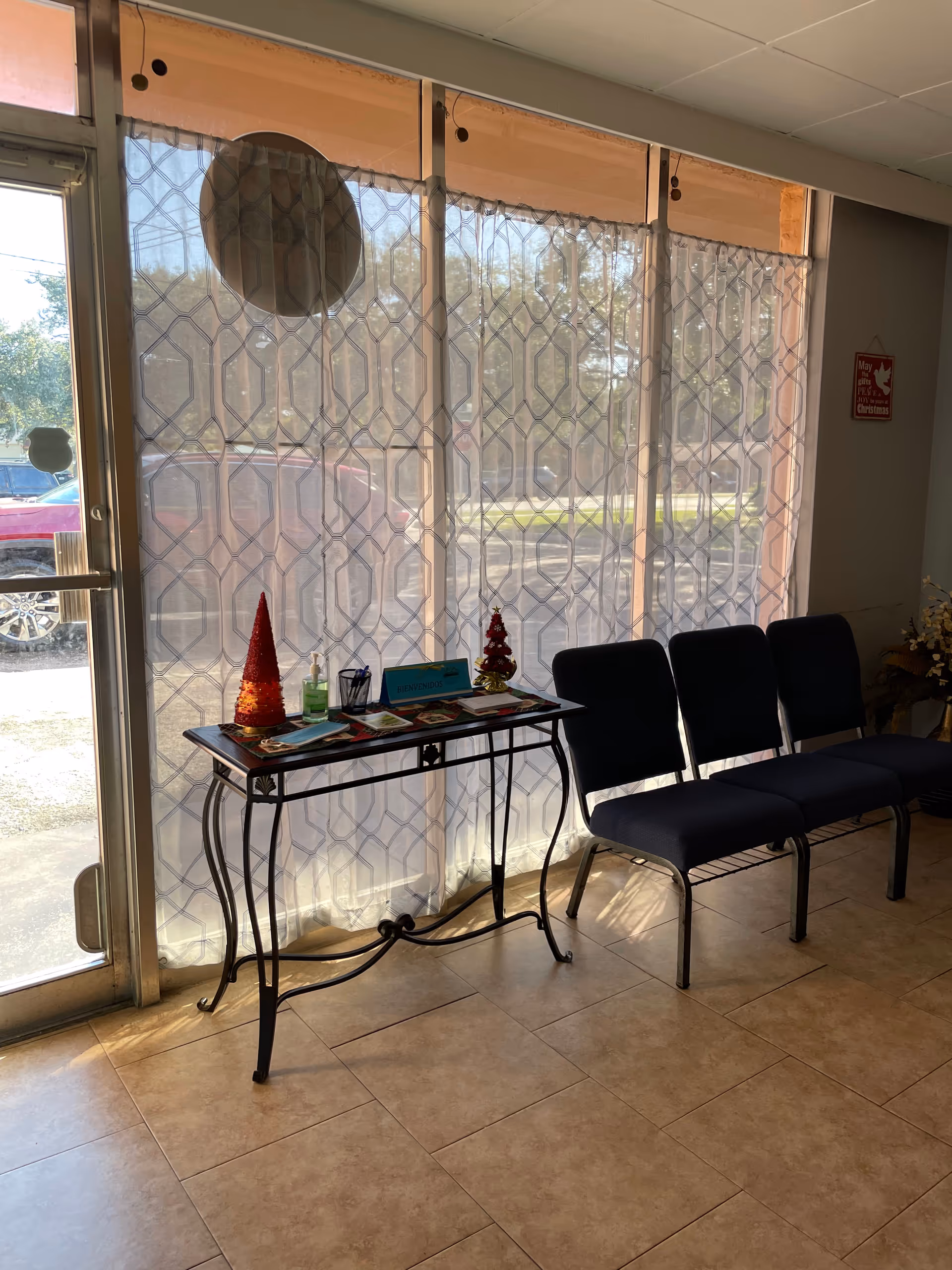 A small lobby with a glass door, patterned curtains, and a table of brochures beside chairs.