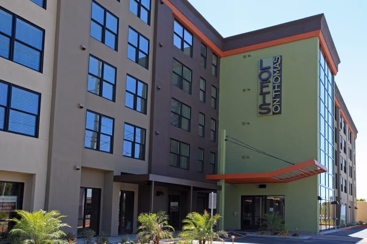 Four-story building with green exterior, large windows, and a red entrance canopy.