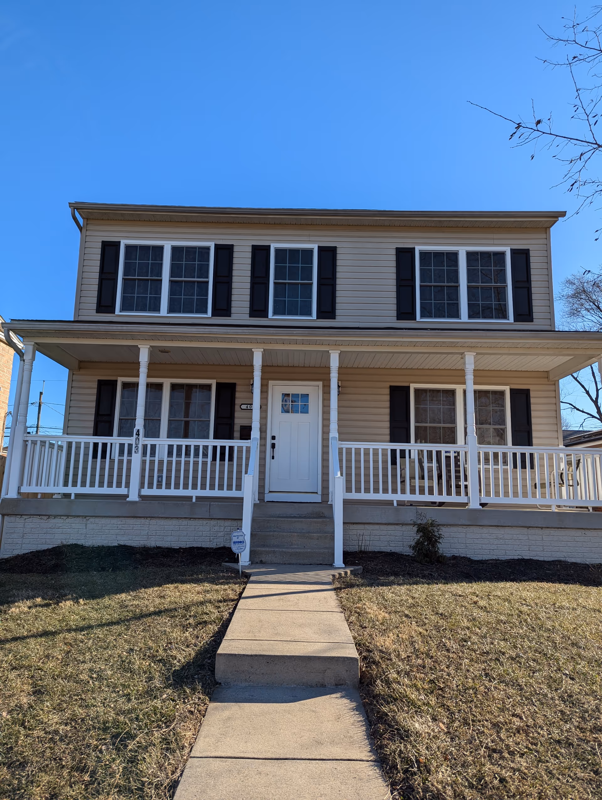 Two-story beige house with a wide front porch and white railings.