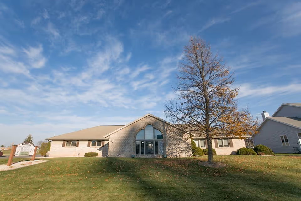 Exterior view of Scandinavian Court Assisted Living building with arched entrance and tree in front.