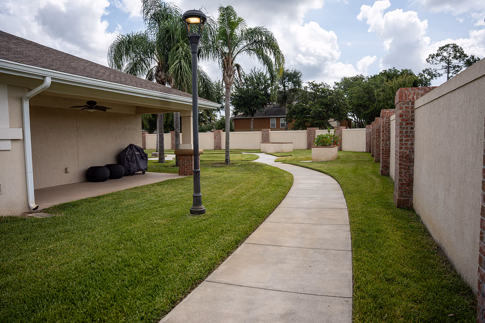 Curved concrete walkway through Memory Lane Cottage's grassy courtyard with a lamppost and brick walls.