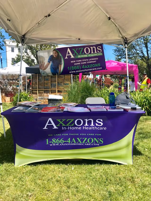 Outdoor Axzons Home Care booth with purple banner and brochures under a canopy