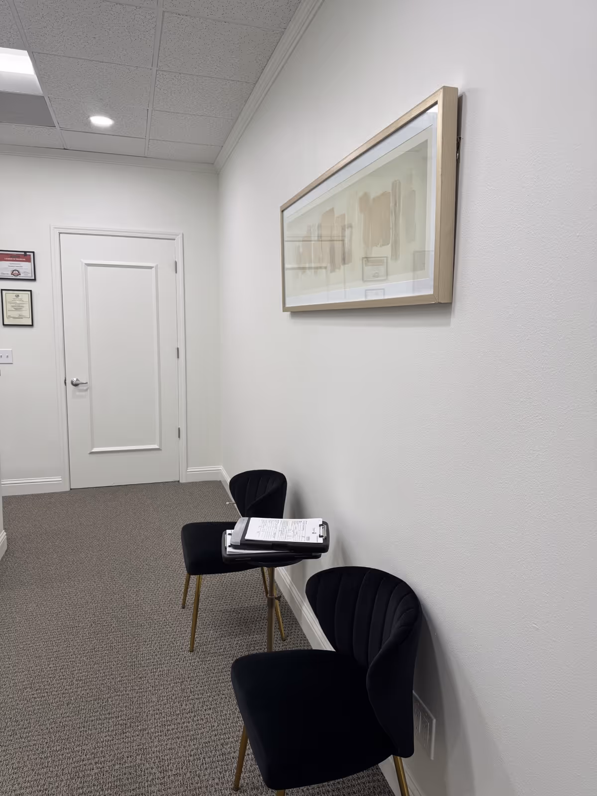 A hallway interior with framed artwork, white walls, and black chairs.