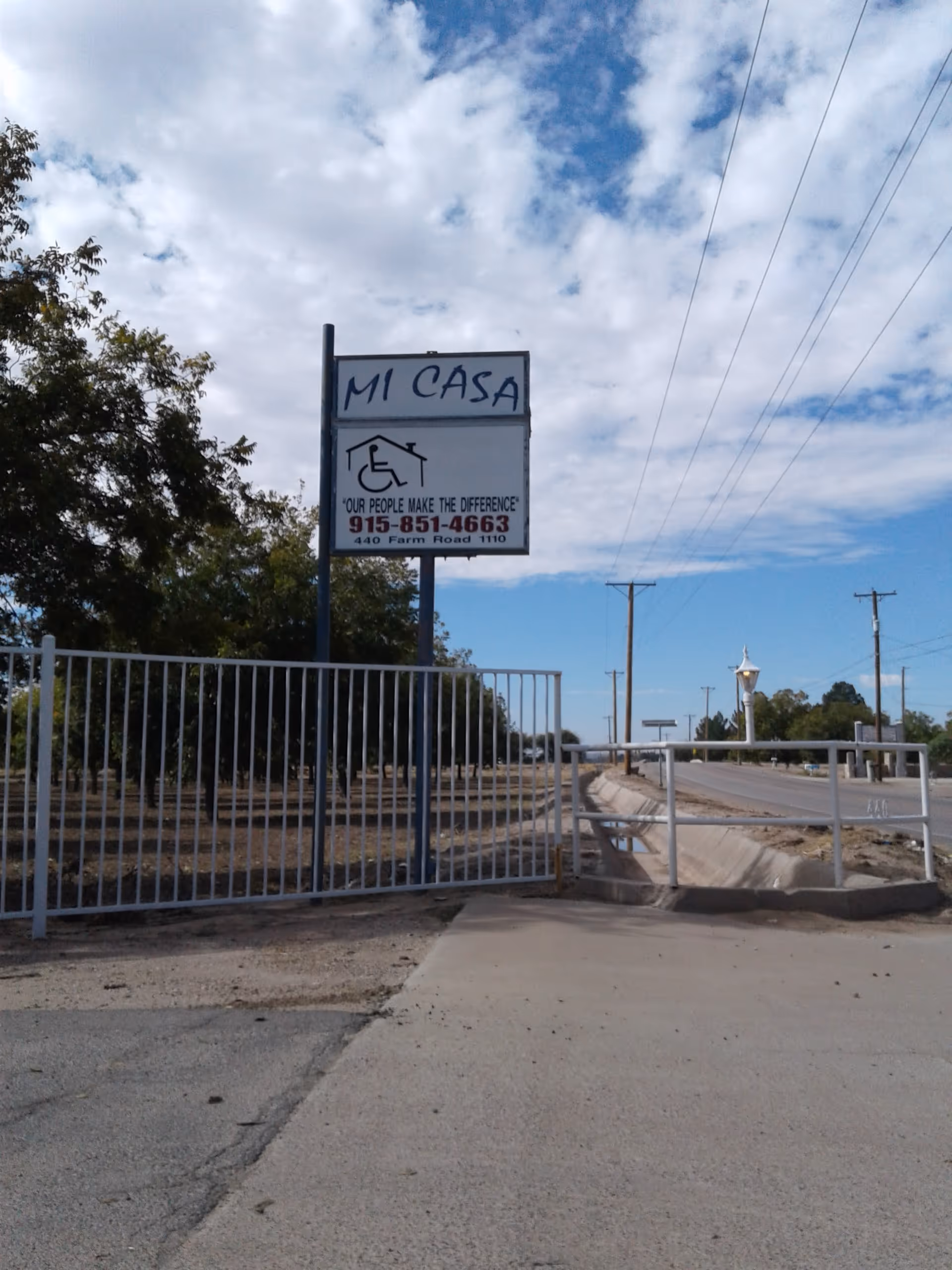 Exterior view of a gated facility sign for Mi Casa, beside a road.