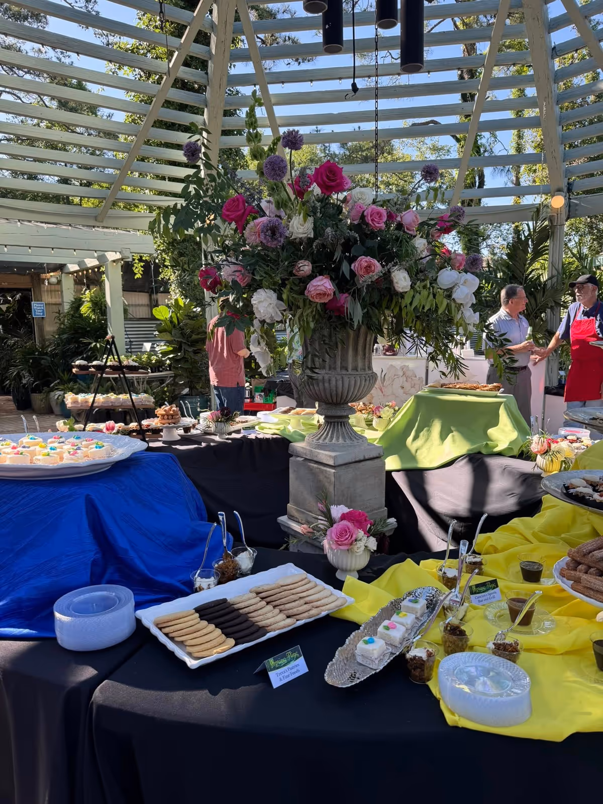 Outdoor catering display with colorful flower centerpiece and dessert tables at a senior home event.