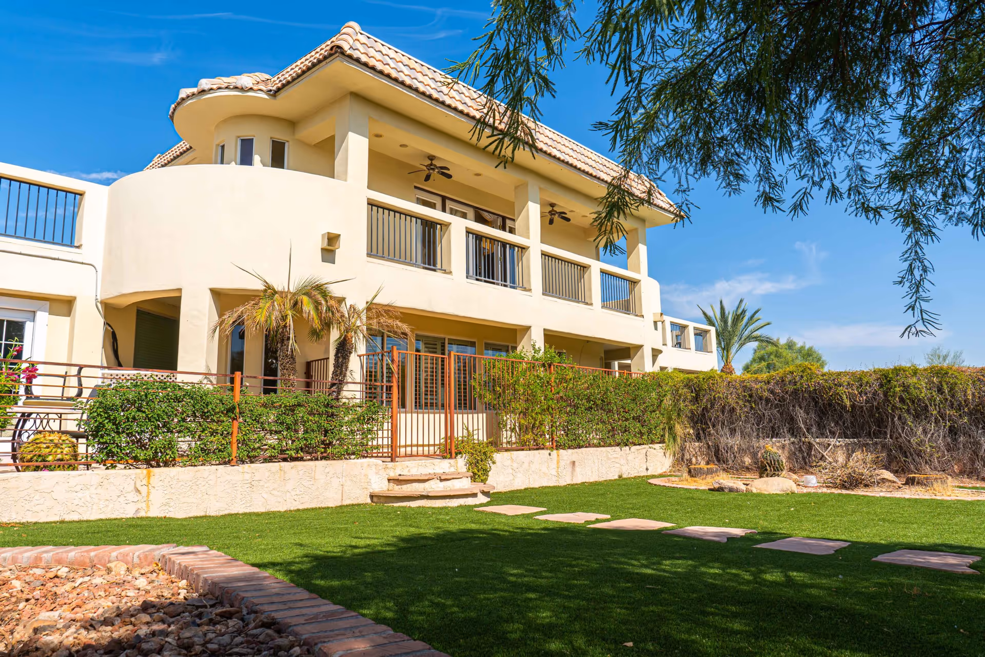 Two-story stucco building with balconies, a fenced patio and a landscaped lawn under a blue sky.
