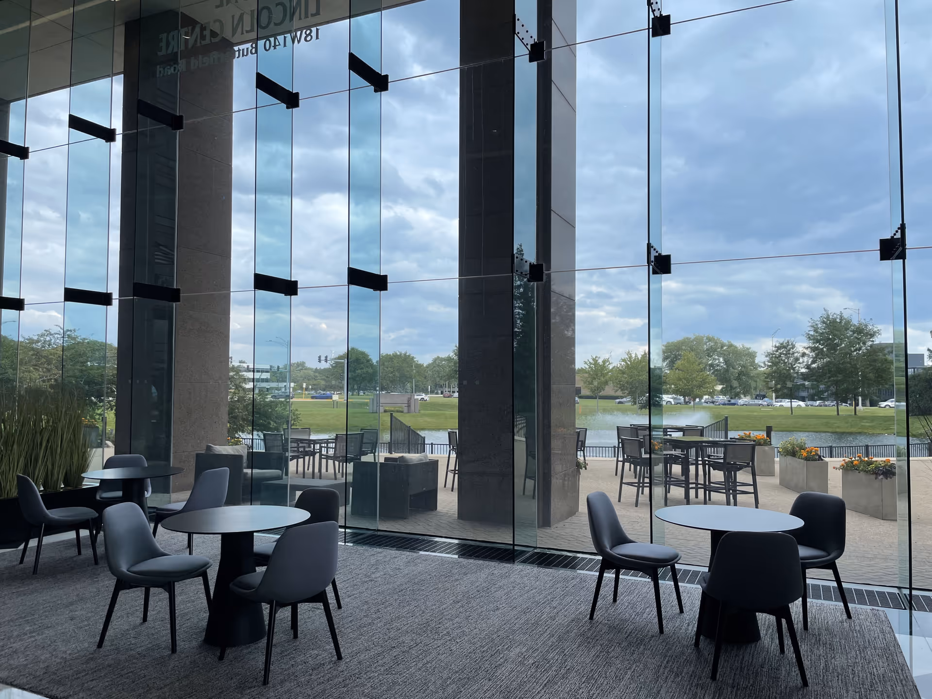 Indoor lounge featuring round tables and chairs beside glass walls open to an outdoor patio.