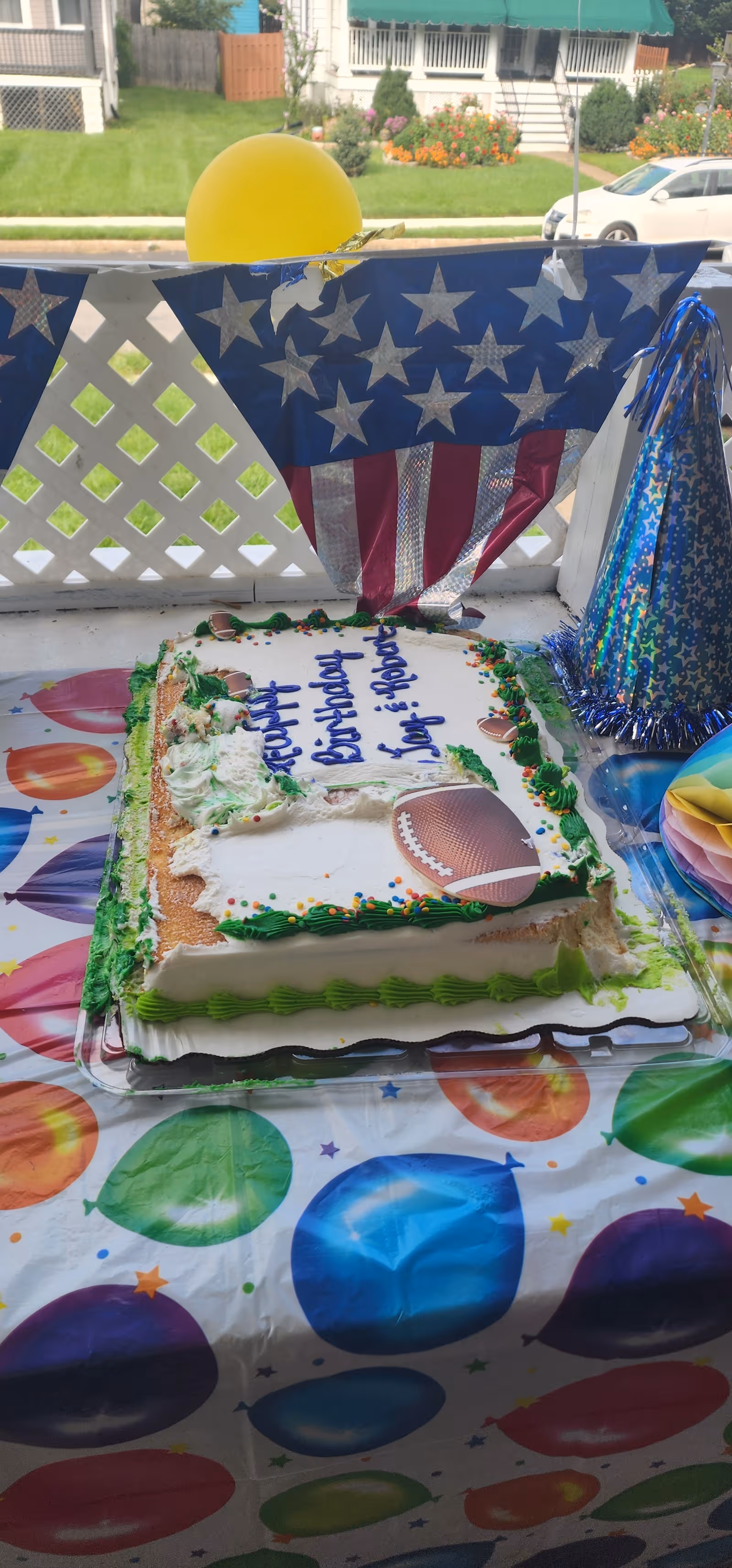 Outdoor porch table with football-themed birthday cake, balloons, and star-spangled decorations.