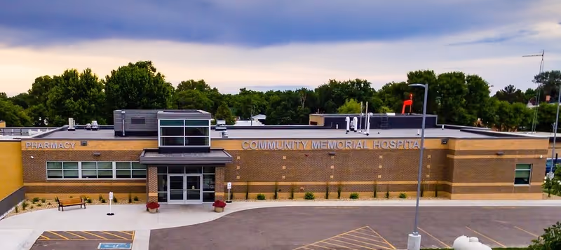 A brick Community Memorial Hospital building seen from a parking lot with trees nearby.