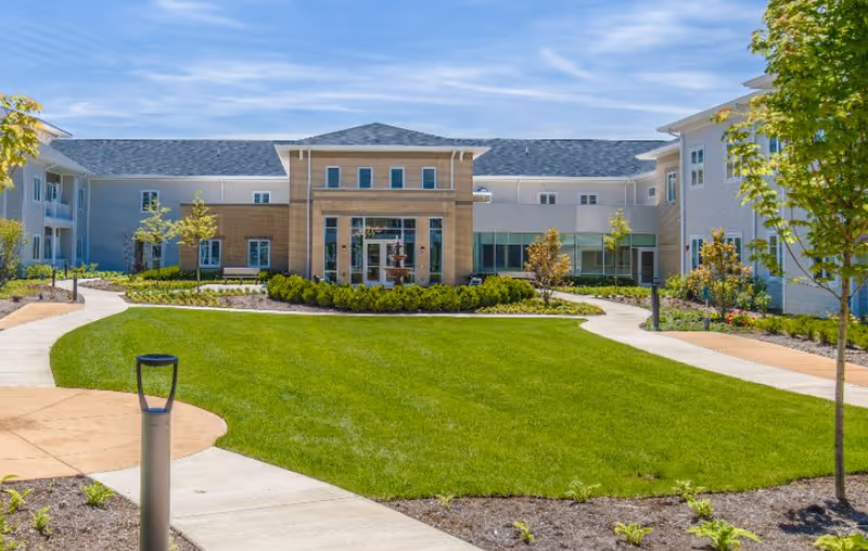 Front exterior view of a senior living facility with a manicured lawn and paths.