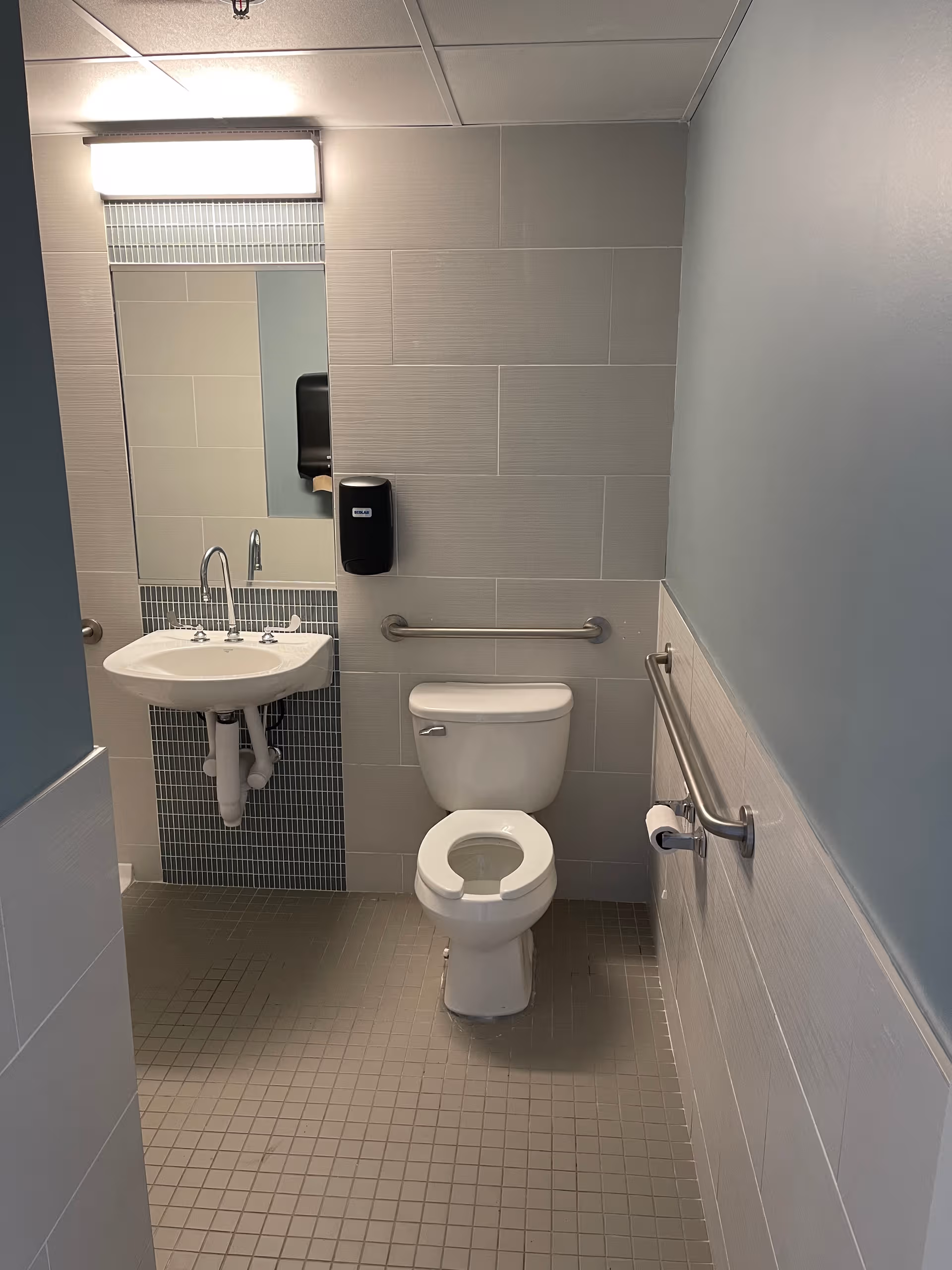 Accessible bathroom with sink, toilet, mirror, and grab bars.