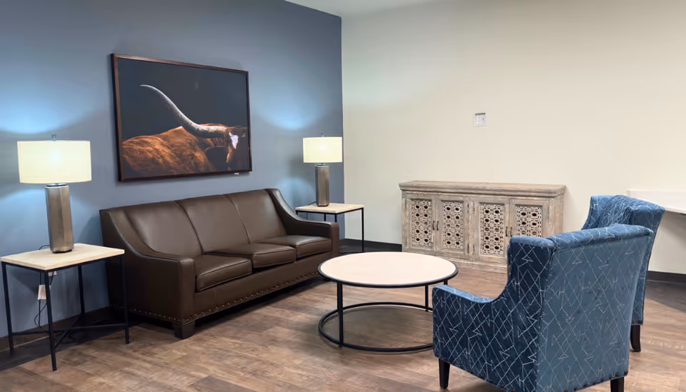 A cozy living room with a brown leather sofa, blue chairs, and wall art.
