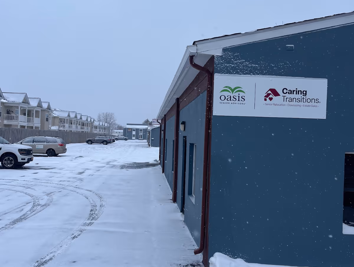 Snowy exterior of Oasis Senior Advisors building with signs and nearby parked cars.