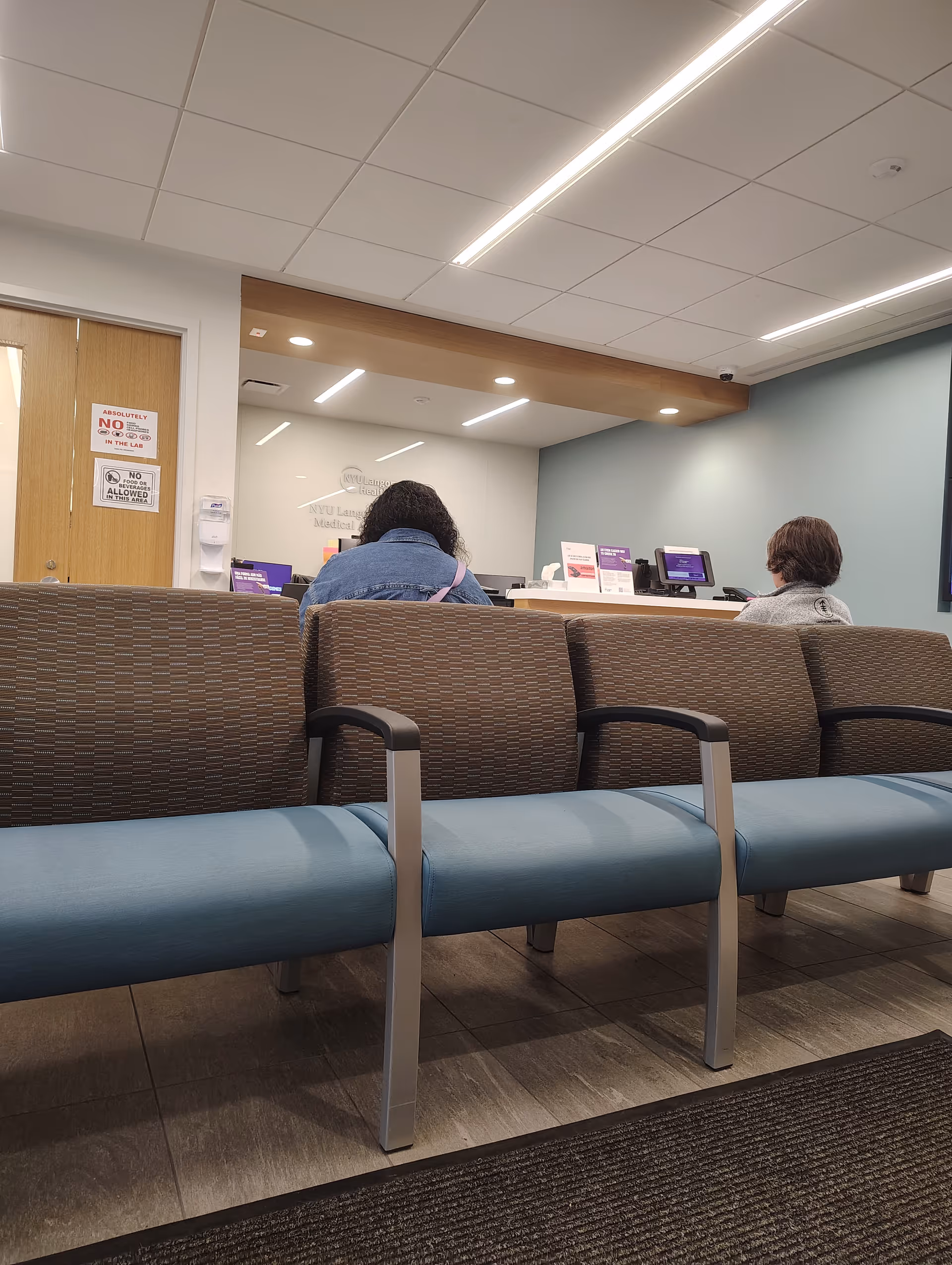 Inside NYU Langone Brooklyn Medical Arts Pavilion waiting area with blue chairs and a reception desk