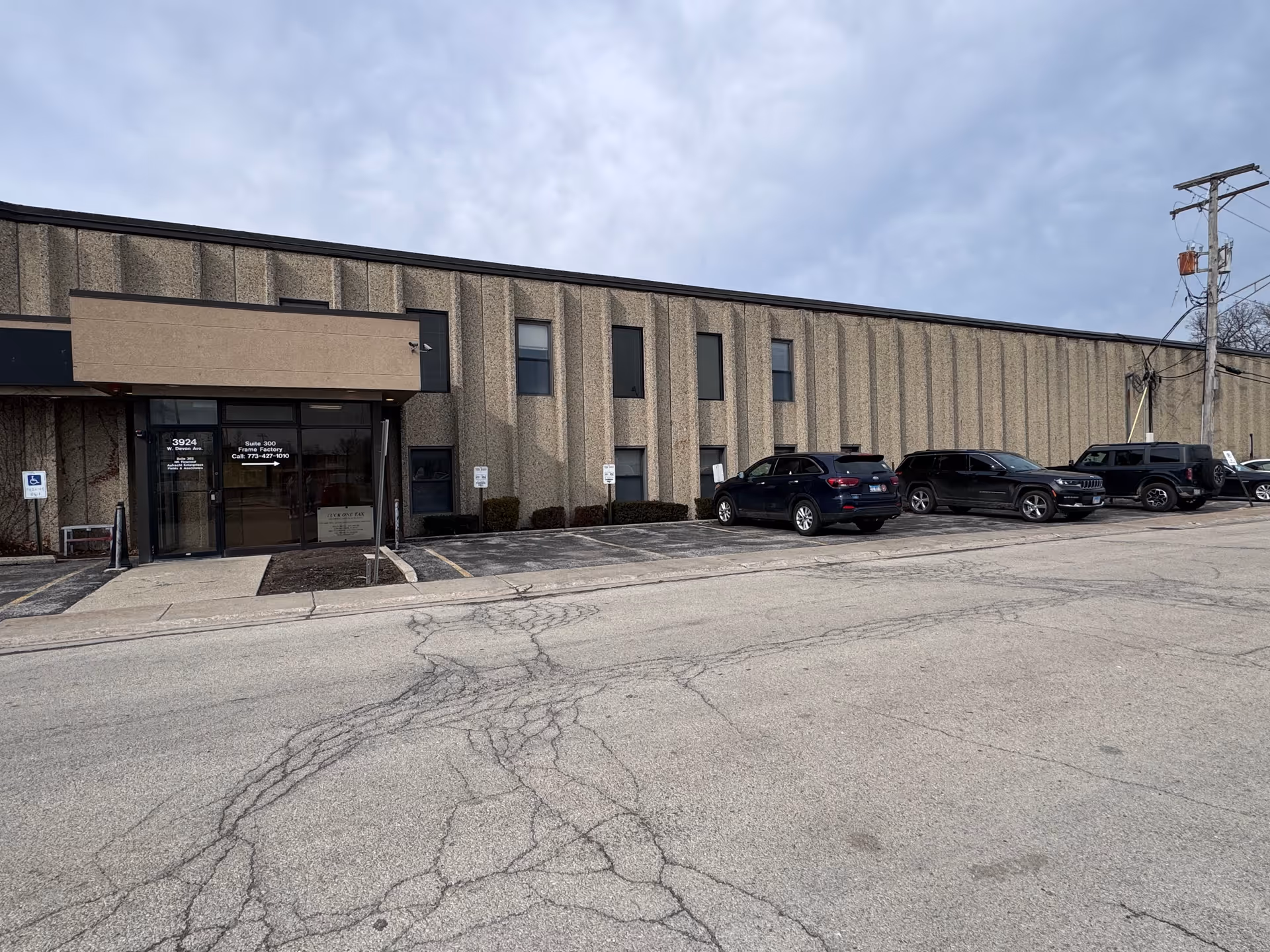 Exterior view of a long beige building with a glass entrance and parked cars.