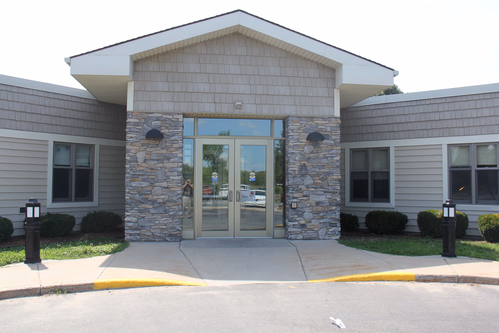 Nursing home entrance with glass doors, stone pillars, and surrounding shrubs