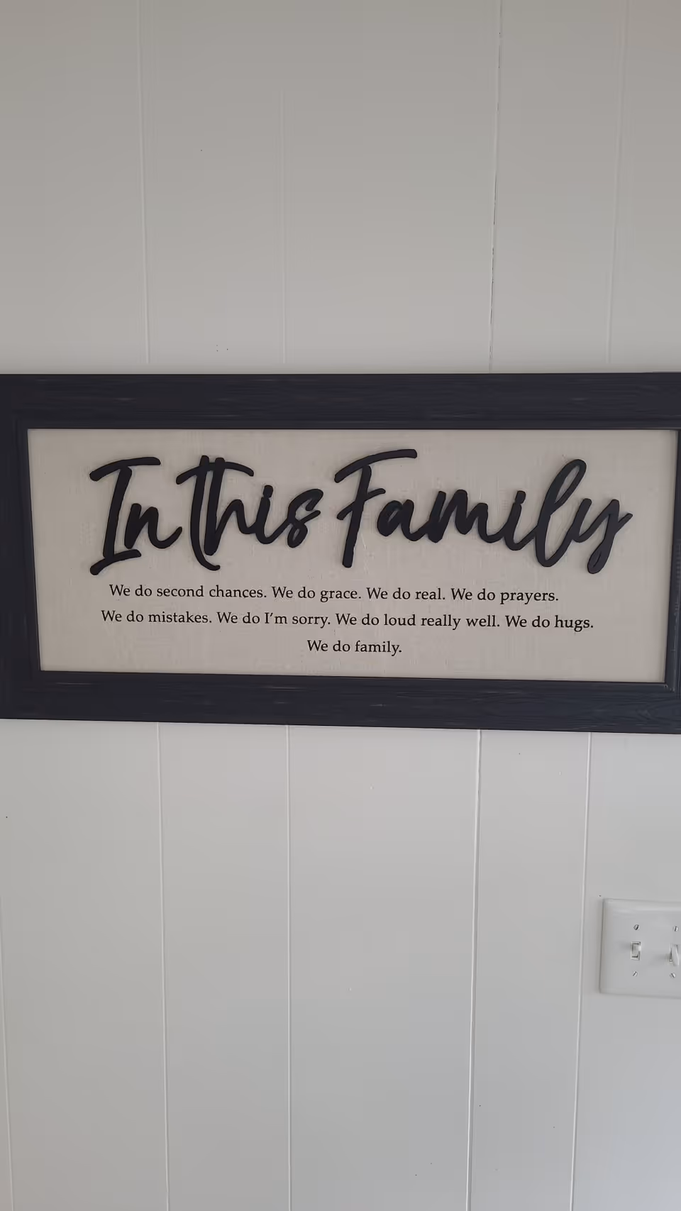 Framed wall sign reading 'In This Family' on a white paneled interior wall