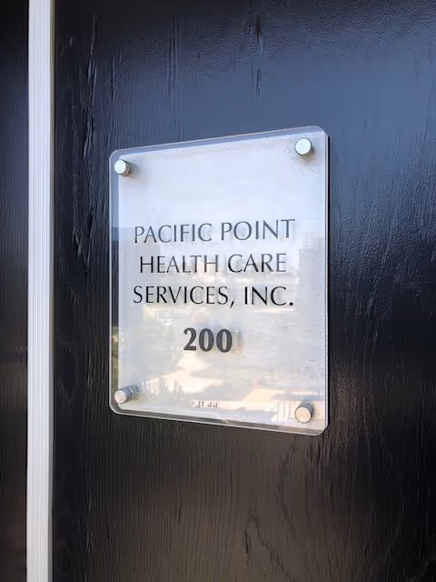 Metal plaque on a dark door reading Pacific Point Health Care Services, Inc. 200