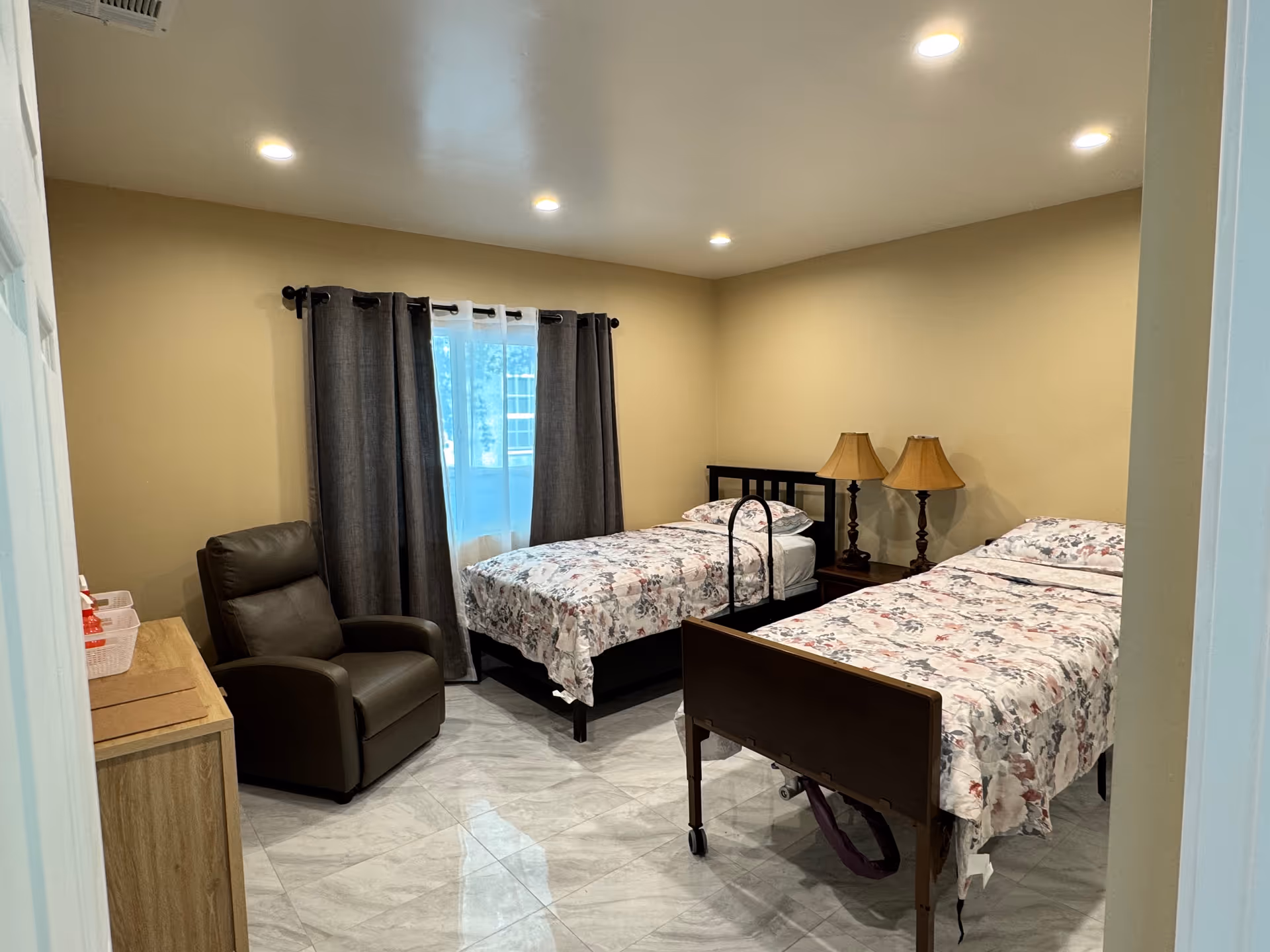 Two twin beds with floral bedding, a chair, and lamps in a beige bedroom.