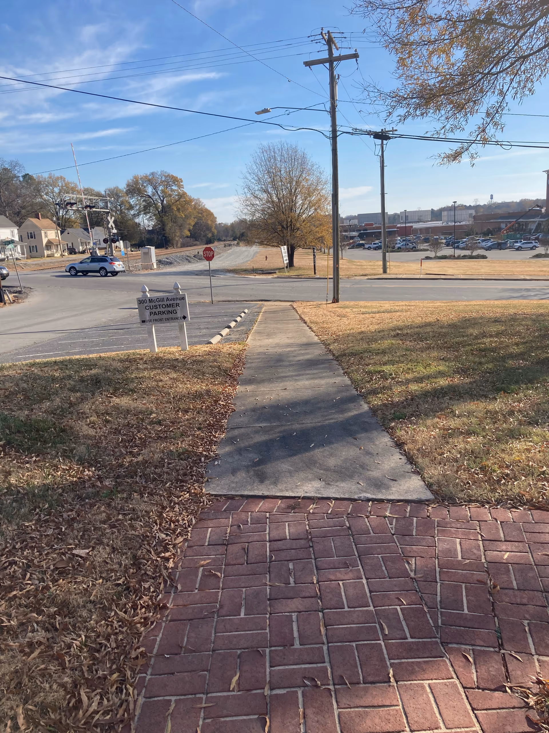 Brick-paved foreground leads to a sidewalk and street with trees and utility poles.