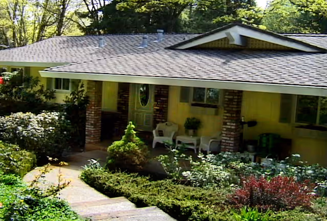 Single-story senior living facility with brick pillars, a covered porch, chairs, and a garden.