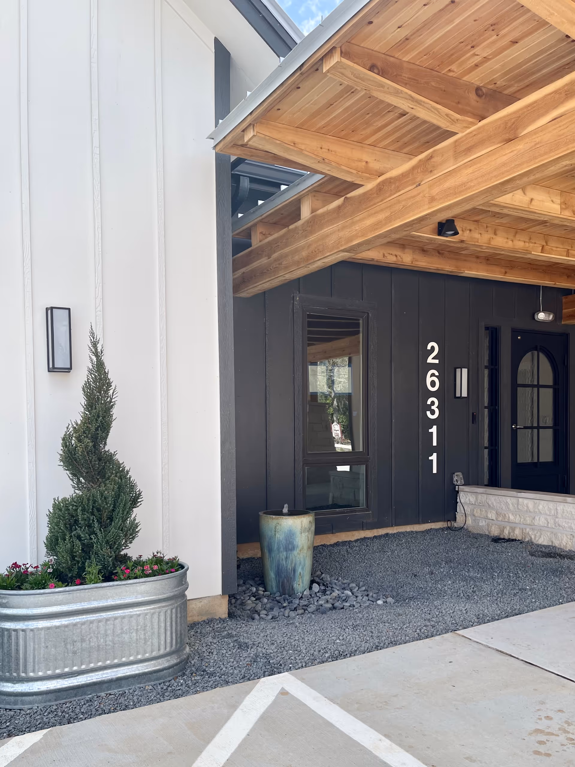 Exterior view of The Woodlands Memory Care and Assisted Living entrance with wooden awning and planters.